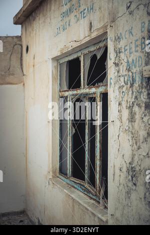 Ein kaputtes Fenster eines ehemaligen Cafés in einem verlassenen Gebäude in der Altstadt von Marpissa, Paros, Griechenland Stockfoto
