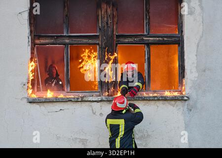 Ein Feuerwehrmann rettet ein Baby aus einem brennenden Gebäude. Der Feuerwehrmann ist in Aktion und rettet das Kind aus der Notsituation. Dieses Bild kann verwendet werden, um Themen von Tapferkeit, Rettungseinsätzen und Rettungsdiensten zu veranschaulichen. || Modell freigegeben Stockfoto