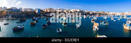 Blick aus der Vogelperspektive auf den Hafen von Marsaxlokk mit Luzzu-Booten und Kirche Stockfoto