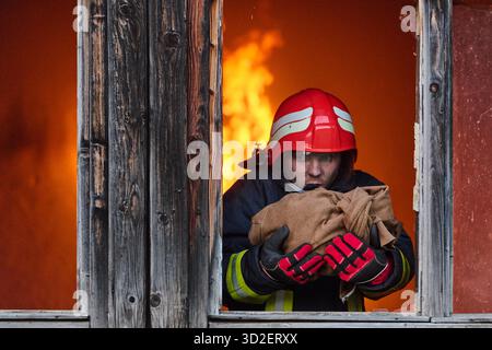 Ein Feuerwehrmann rettet ein Baby aus einem brennenden Gebäude. Der Feuerwehrmann ist in Aktion und rettet das Kind aus der Notsituation. Dieses Bild kann verwendet werden, um Themen von Tapferkeit, Rettungseinsätzen und Rettungsdiensten zu veranschaulichen. || Modell freigegeben Stockfoto