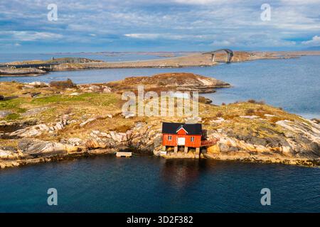 Kleines Haus eingebettet auf felsiger brauner Insel zwischen ausgedehnten Fjordgewässern der norwegischen Küste. Die Berge zeigen die dramatische natürliche Schönheit Norwegens Stockfoto