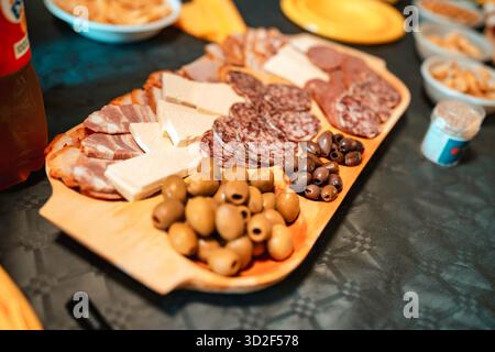 Hölzerne Serviertafel mit verschiedenen Wurstwaren, in Scheiben geschnittenen Käseblöcken und schwarzen und grünen Oliven, die einen einladenden Aufstrich für einen A schaffen Stockfoto