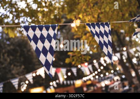 Bayerische Rautenflaggen und warme Lichterketten schmücken eine Veranstaltung im Freien, bei der Bier, Tradition und Gemeinschaft gefeiert werden und eine festliche deutsche Atmosphäre schaffen Stockfoto