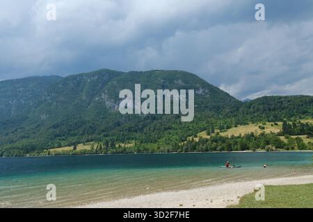 Menschen, die Freizeitaktivitäten am Ufer des Bohinj-Sees mit Kajak auf türkisfarbenem Wasser genießen, Julischen Alpen, Triglav-Nationalpark, Slowenien. Stockfoto