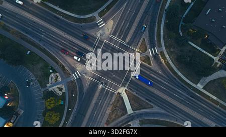 Drohnenblick auf beleuchtete Ampeln und Autos an einer großen Kreuzung am Abend. Stockfoto