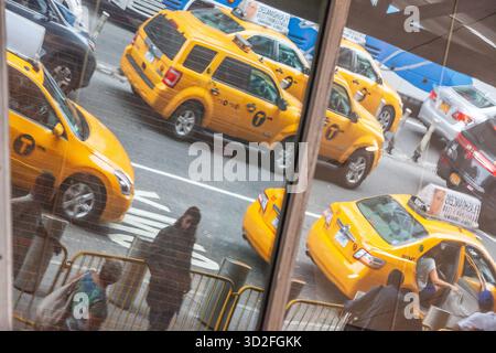 Gelbe Taxis, die während der Hauptverkehrszeit auf einer New Yorker Straße vorbeifahren, spiegeln sich in einem Fenster Stockfoto