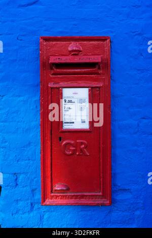 Ein knallroter Briefkasten an einer hellblau bemalten Wand in Downham Market, Norfolk. Stockfoto