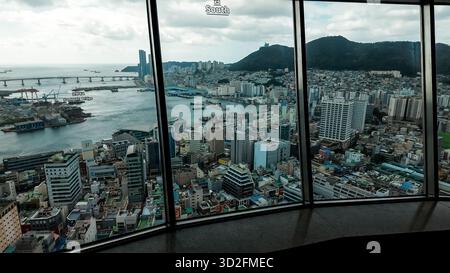 BUSAN, SÜDKOREA - 10. OKTOBER 2025 - Busans Stadtbild und Hafen von einem hohen Fenster mit bewölktem Himmel aus gesehen Stockfoto