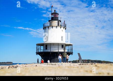 An einem klaren Herbsttag spazieren Besucher entlang der felsigen Mole in Richtung des historischen Spring Point Ledge Lighthouse unter einem hellblauen Himmel Stockfoto