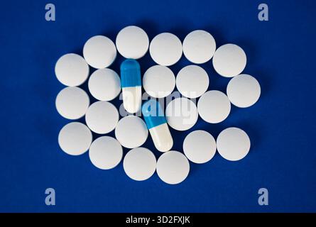 Runde weiße Pillen, die ein kreisförmiges Muster auf blauer Oberfläche bilden. Konzept der Medizin, Pharmazie und Gesundheitswirtschaft. Stockfoto