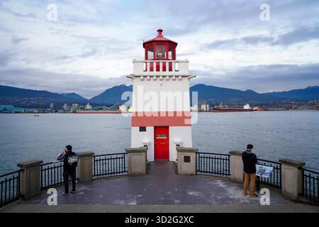Besucher stehen an der Ufermauer neben dem Brockton Point Lighthouse im Stanley Park mit Blick auf den Hafen und die North Shore Mountains. Stockfoto