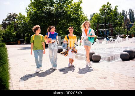 Eine Gruppe verschiedener Teenager, die einen sonnigen Tag im Freien in der Nähe eines Brunnens mit Rucksäcken und einer fröhlichen Atmosphäre genießen Stockfoto