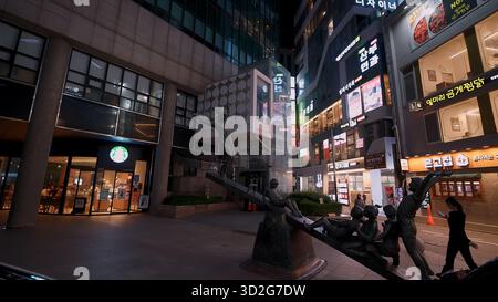 SEOUL, SÜDKOREA - 11. OKTOBER. 2025: Urban Street at Night in Seoul, Südkorea, mit einem Starbucks und einer Skulptur Stockfoto