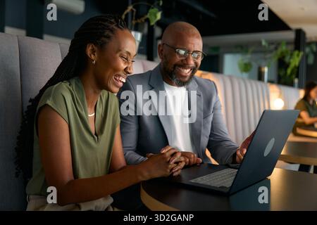 Fröhliche schwarze Geschäftsleute, die am Laptop arbeiten, während sie am Schreibtisch in der Bürolounge sitzen Stockfoto