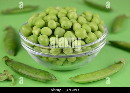 Junge grüne Erbsen in einer Schüssel auf grünem Hintergrund. Nahaufnahme. Stockfoto