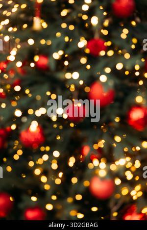 Abstrakter und verschwommener Bokeh-Hintergrund eines Weihnachtsbaums mit leuchtenden goldenen Lichtern und runden roten Weihnachtsschmuck. Stockfoto