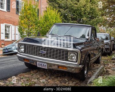 Ein klassischer, dunkelblauer Chevrolet Cheyenne Pickup Truck, der auf einer historischen Kopfsteinpflasterstraße in New Castle, Delaware, mit kolonialen Häusern im Hinterland geparkt wird Stockfoto