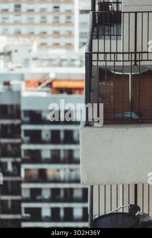 Moderner Stadtbalkon mit Metallgeländer und kleinem runden Tisch im Fokus, Hochhäuser, die sanft im Hintergrund verschwimmen, aufgenommen mit Teleobjektiv Stockfoto