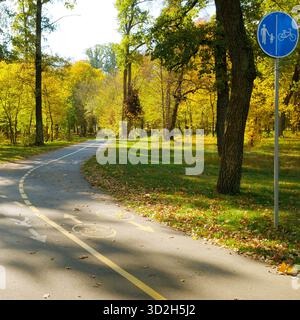 Ein deutlich gekennzeichneter gemeinsamer Fahrrad- und Fußgängerweg schlängelt sich durch einen wunderschönen Park mit Bäumen, die hellgelb und grün im Herbst sind. Stockfoto