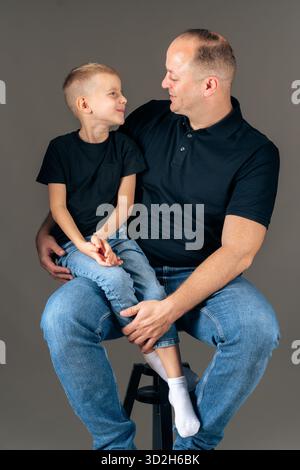 Vater und Sohn sitzen dicht und betrachten einander ein warmes emotionales Studio-Porträt über Familienbindung Stockfoto