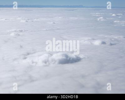 Über Den Wolken: Heiterer Himmel Und Weiße Wolkenlandschaft Aus Großer Höhe. Ein ruhiger Blick aus der Luft über einem riesigen Wolkenmeer mit einem fernen Berg Stockfoto