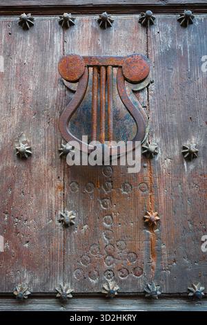 Handgefertigter Türklopfer aus Eisen, in leierähnlichem Design geformt und auf einer verwitterten Holztür montiert Stockfoto