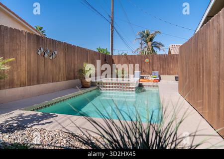 Swimmingpool mit gefliestem Spa in einem kleinen umzäunten Hinterhof mit Liegestühlen, Palmen und Pflanzen Stockfoto