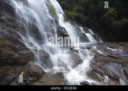 Der mächtige Wasserfall fließt über dunkle, nasse Felsen im grünen tropischen Wald. Rauschendes Wasser schafft eine ruhige und fesselnde Naturlandschaft, die an Fühlungen erinnert Stockfoto