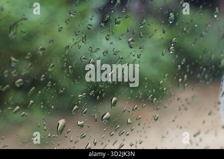 Moody abstrakter Hintergrund von Regenwassertropfen auf Fensterglas. Grüne Natur im Freien sorgt für ruhige und feuchte Wetterszenen, perfekt für friedliche oder traurige Gäste Stockfoto