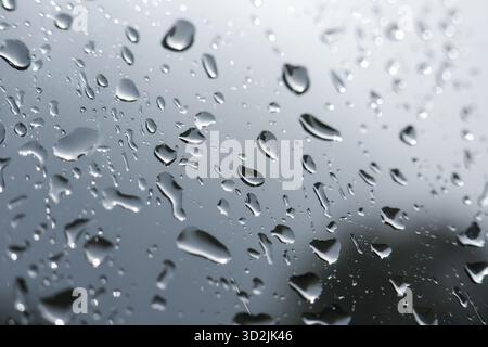 Melancholischer Blick auf Regentropfen und reines Wasser auf nassem Fenster. Graues, düsteres Wetter erzeugt einen abstrakten Hintergrund mit Kondensation auf transparentem Hintergrund Stockfoto