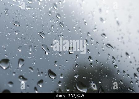 Trauriger, melancholischer Blick auf Regentropfen auf Fensterglas. Grauer, abstrakter Hintergrund mit Kondensation sorgt bei stürmischem Wetter für ein düsteres Gefühl Stockfoto