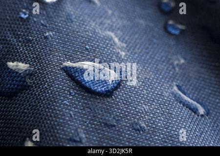 Makroaufnahme von Wassertröpfchen, die auf blauem wasserdichtem Gewebe perlen. Diese detaillierte Texturaufnahme zeigt wasserabweisende Qualität strapazierfähiger Textilmateri Stockfoto