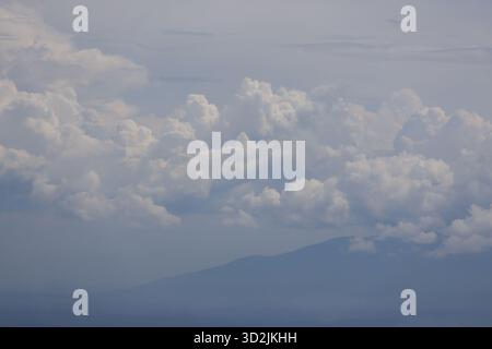 Flauschige weiße Cumulus-Wolken ziehen friedlich über den weiten blauen Himmel und bilden eine weitläufige, ruhige Kulisse über fernen, ruhigen Bergen. Szene ev Stockfoto