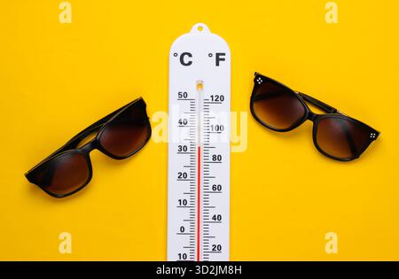 Sommerferienkonzept. Wetterthermometer mit Sonnenbrille auf gelbem Hintergrund. Draufsicht Stockfoto