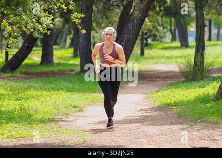 Foto einer Frau, die im Park läuft, Sportkleidung trägt und lächelt Stockfoto