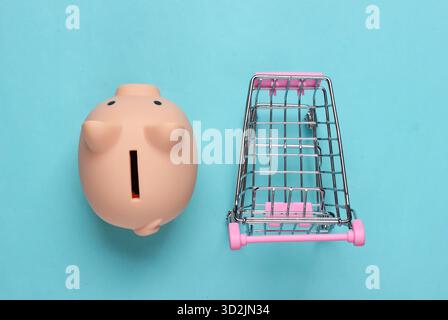 Schweinebank und Mini-Supermarkt-Trolley auf blauem Pastellhintergrund. Minimalistische Studioaufnahme. Draufsicht. Flache Lagen. Stockfoto