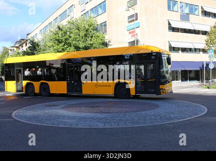Karlstad, Schweden-17. September 2025: Gelber öffentlicher Bus mit Passagieren an Bord, die auf der Straße am großen Gebäude mit Schildern und Bäumen fahren Stockfoto