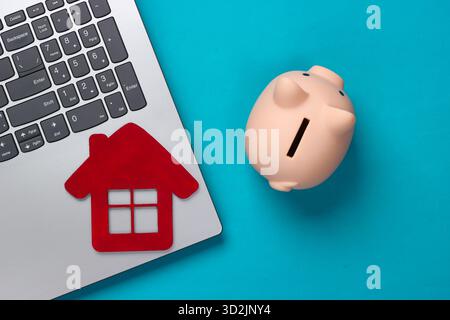 Sparen Sie für das Wohnen. Laptop, Schweinebank mit Hausfigur auf blauem Hintergrund. Draufsicht Stockfoto