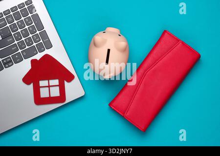 Sparen Sie für das Wohnen. Laptop, Schweinebank mit Hausfigur, Brieftasche auf blauem Hintergrund. Draufsicht Stockfoto