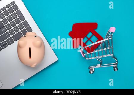 Sparen Sie für das Wohnen. Laptop, Schweinebank, Einkaufswagen mit Hausfigur, Brieftasche auf blauem Hintergrund. Draufsicht Stockfoto