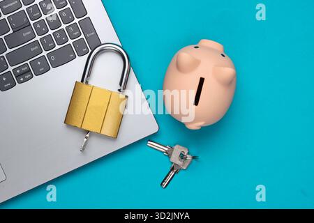 Laptop mit Schlüsseln und Schloss, Schweinebank auf blauem Hintergrund. Draufsicht Stockfoto