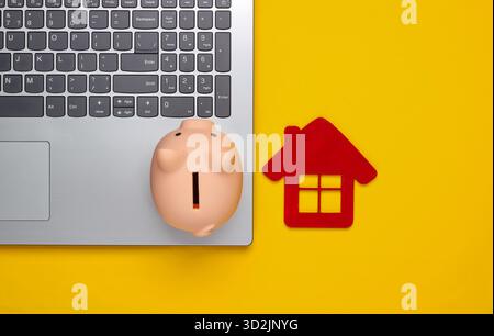 Sparen Sie für das Wohnen. Laptop, Schweinebank mit Hausfigur auf gelbem Hintergrund. Draufsicht Stockfoto