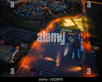 Nächtlicher Blick auf den Circus Renz, ein heller Skatepark und gestreifte Zelte leuchten neben organisiertem Busparkplatz, Wohnraster und warmer Straße Stockfoto