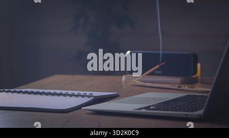 Abendbilanz. Bluetooth-Lautsprecher gibt leise Musik in der Nähe von Computer und Notebook wieder, Weihrauch brennt langsam, Lampen werfen goldenes Licht der Ruhe Stockfoto