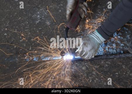 Nahaufnahme von Schweißerhandschuhen, die intensiv auf Metall arbeiten, Funken fliegen Stockfoto