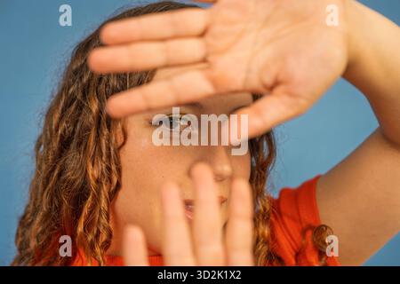Eine junge Frau, die durch ihre Hände blickt, ihr Gesicht bedeckt und schüchtern oder neugierig aussieht Stockfoto