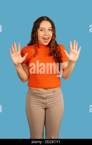 Eine junge Frau mit lockigem Haar, die zehn Finger zeigt und Überraschung und Aufregung ausdrückt Stockfoto