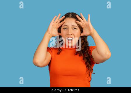 Eine Frau fühlt sich gestresst, hält die Hände an den Kopf vor blauem Hintergrund Stockfoto