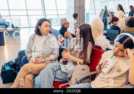 ALMATY, KASACHSTAN - 18. AUGUST 2025: Drei junge Frauen sitzen in einem Wartebereich am Flughafen. Sie führen Gespräche. Stockfoto