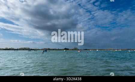 Bosham Harbour, West Sussex, England, bei Flut mit einem vertäuten Holzboot und einem überfluteten Damm-Schild unter einem hellblauen Himmel mit Wolken Stockfoto
